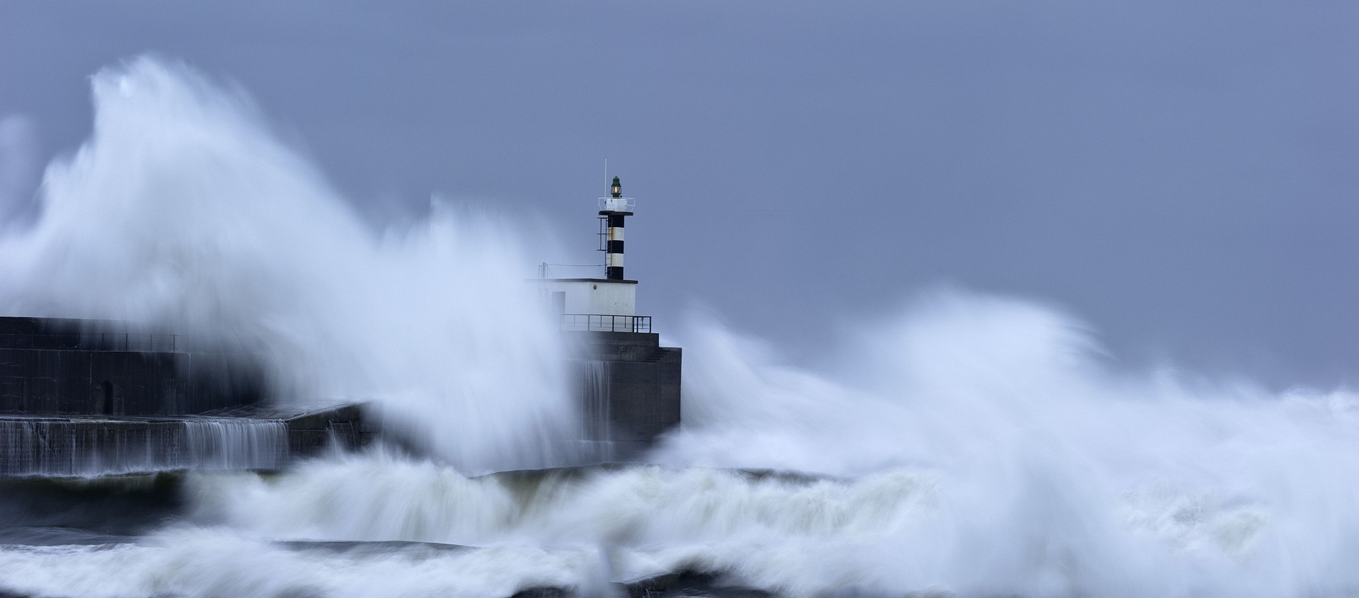 Temporal en San Esteban de Pravia con las olas sobrepasando el dique de contención y el faro del puerto.