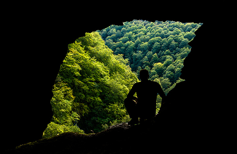 Silueta de hombre en una cueva con forma de hoja mirando el bosque cantábrico