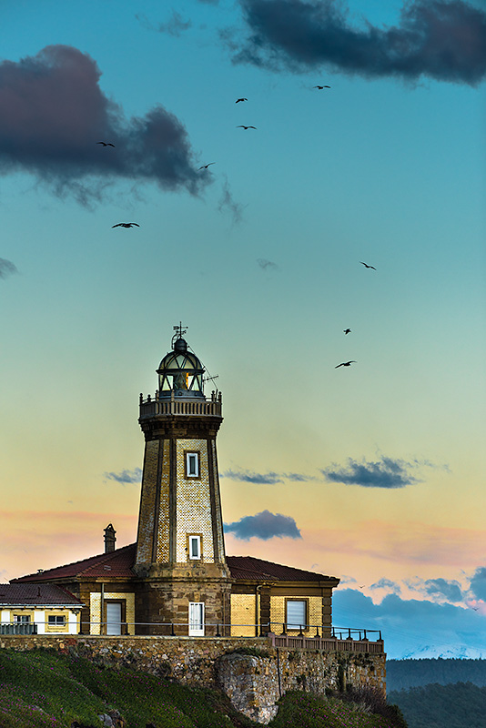 Fotografía del edificio y linterna del faro de San Juan de Nieva con un cielo limpio de nubes y gaviotas