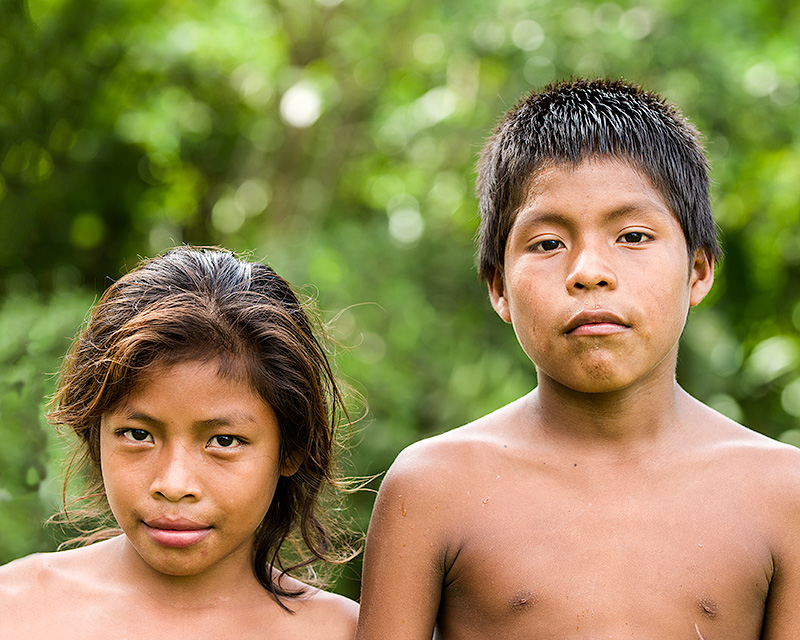 Fotografía de un niño y una niña emberás. Ambos miran a la cámara con mirada segura. La niña es más pequeña.