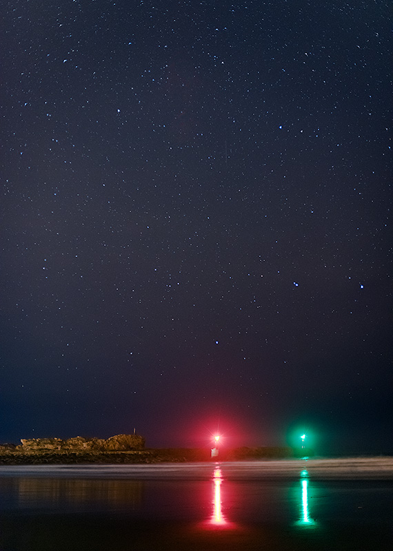 Noche en el faro de San Vicente de la Barquera. Asturias. Lasbalizas de posición verde y rojo de la entrada de la ría destacan sobre un mar en calma y un cielo despejado.