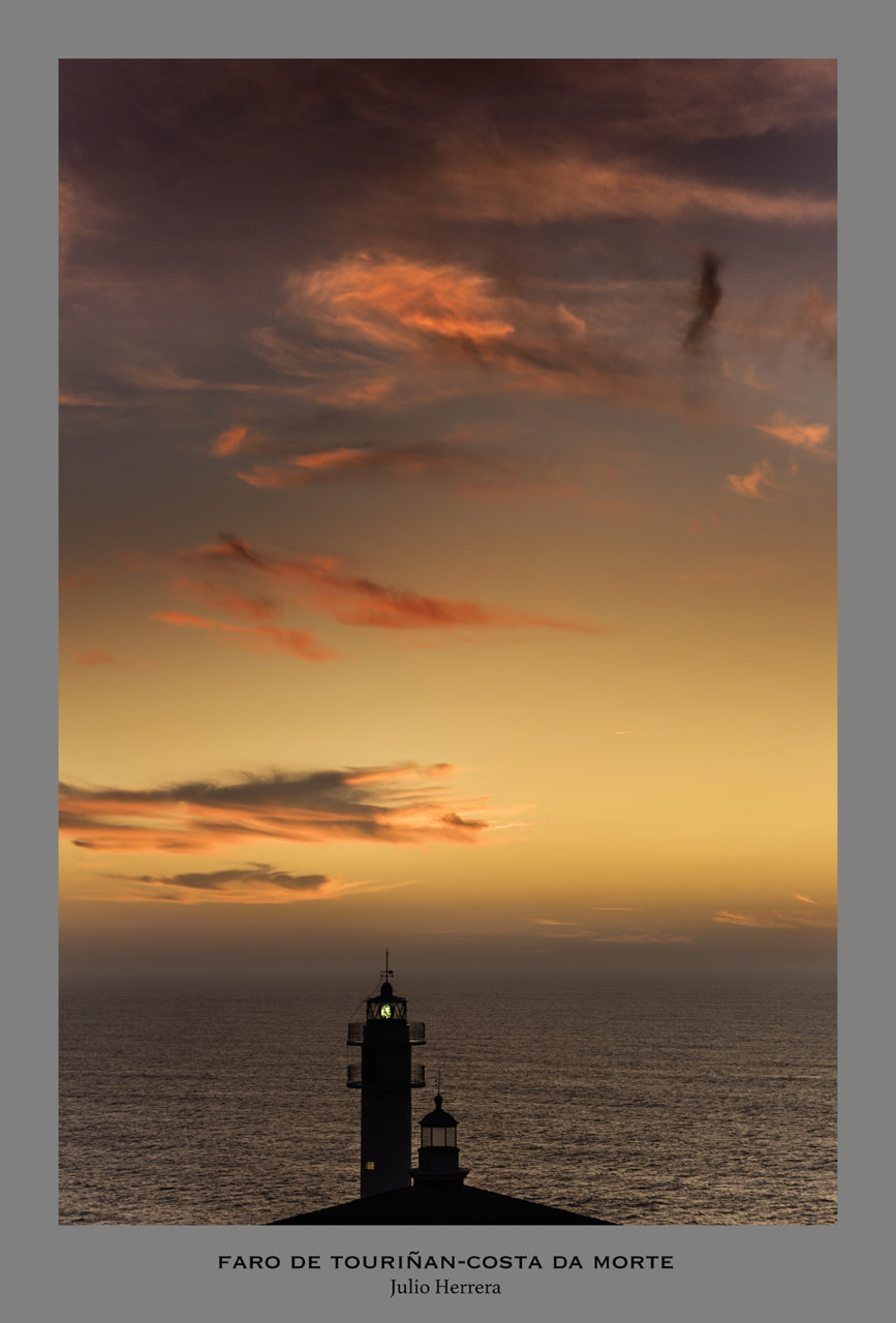 Fotografía del faro de Tourñan en la costa da morte, Galicia al atardecer. Se ve la linterna del faro encendida y al fondo el mar y el horizonte en unos tonos naranjas y amarillos en un cielo con alguna nube
