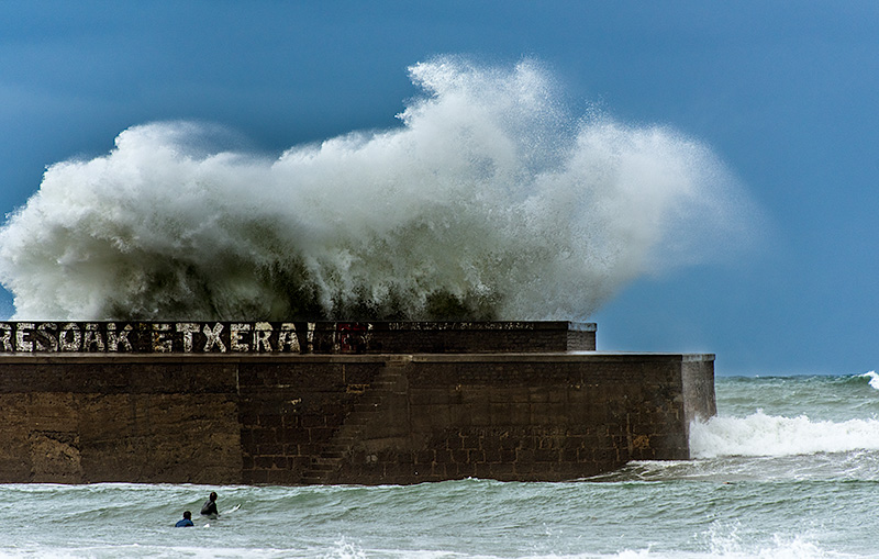 Olas que sobrepasan el muro del dique de La Gallarda portua en Plentzia donde esperan dos surfistas.